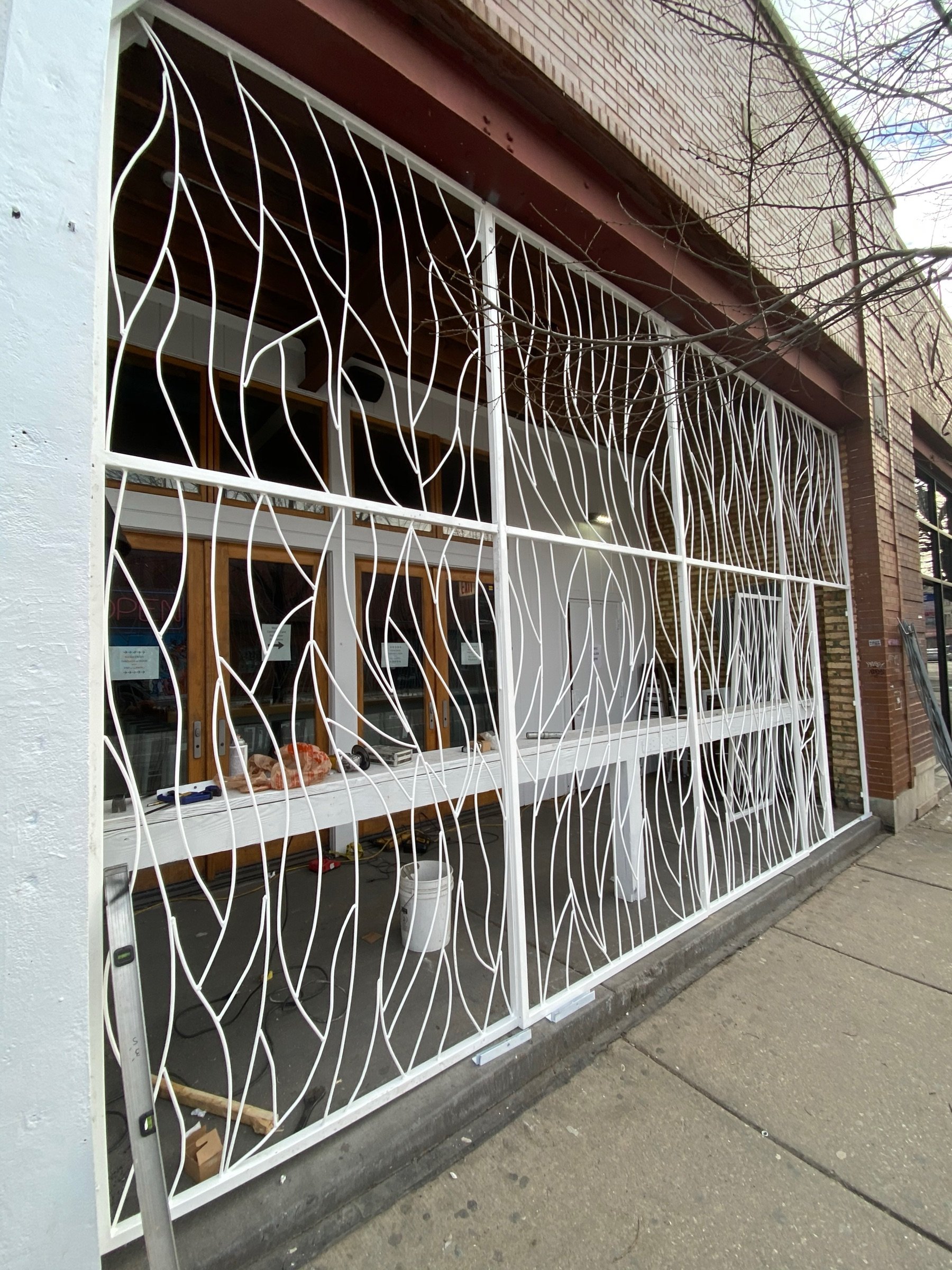 Wide view of the Moca storefront facade with vine-pattern metalwork across the street-facing glazing