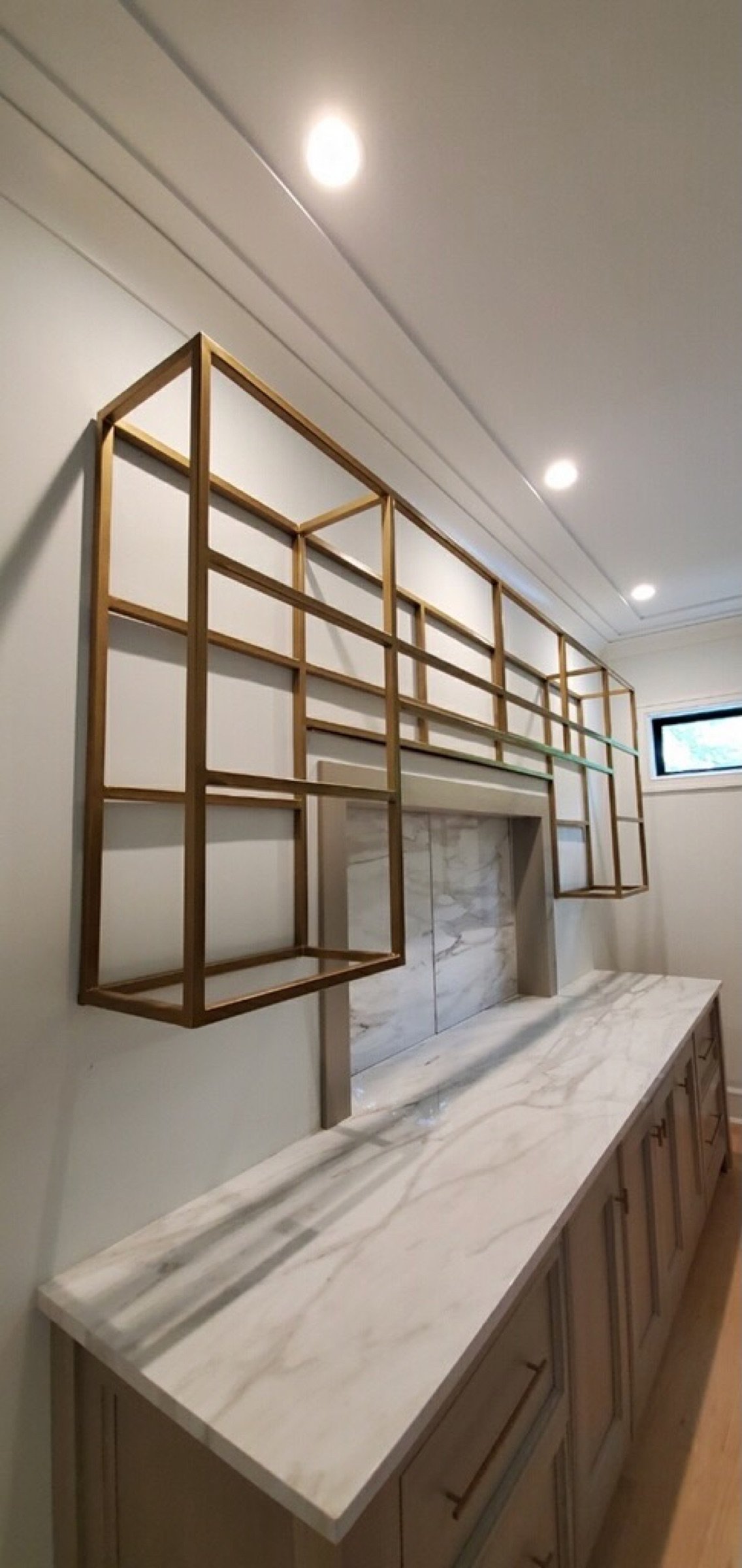 Left-side angle of the gold-finished steel shelving above the marble counter