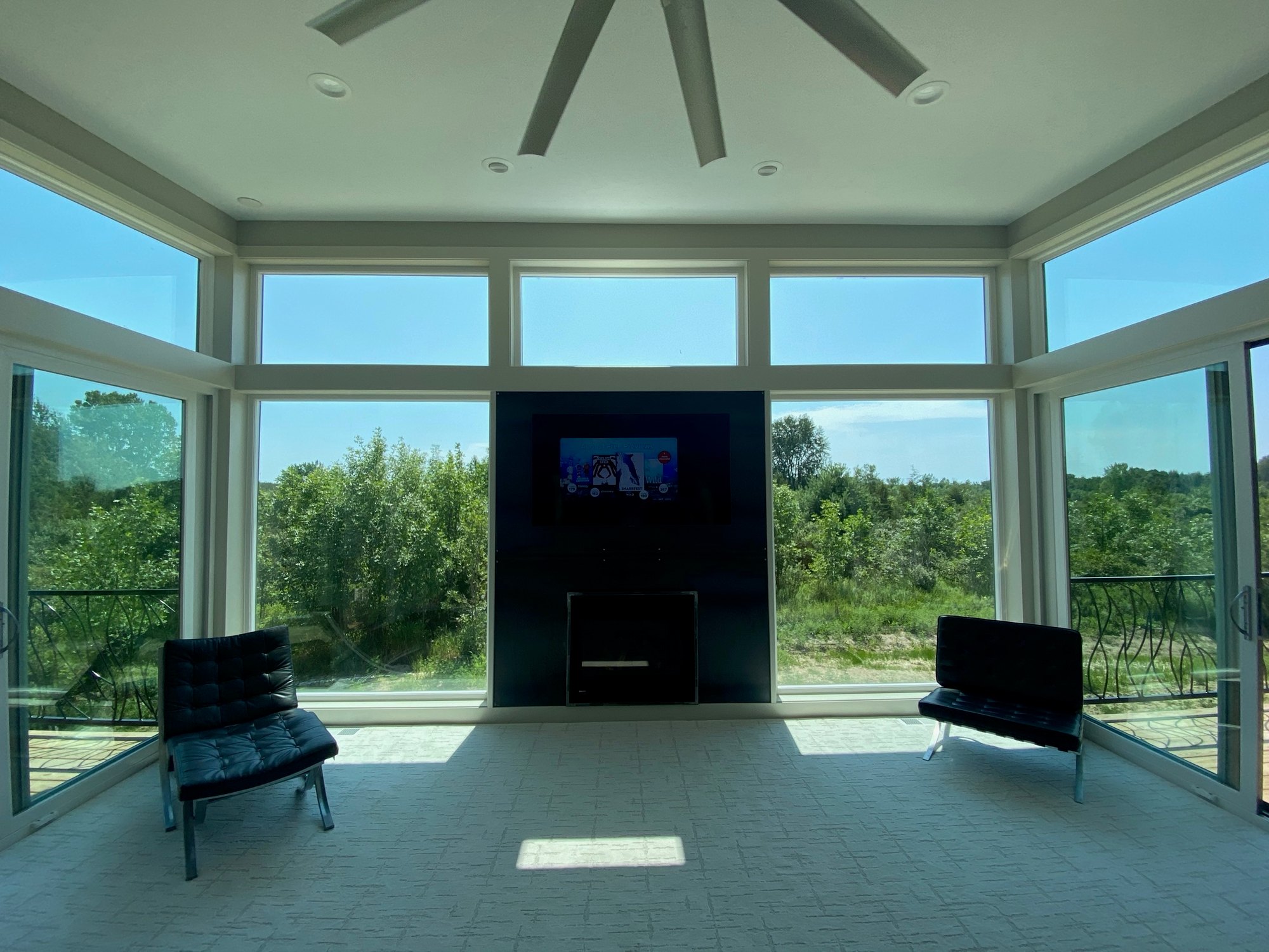 Sun-filled room with a custom floor-to-ceiling black-steel fireplace surround, Barcelona chairs, and hand-forged iron railings visible through full-height windows